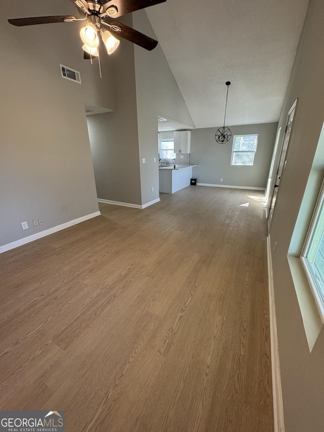 unfurnished living room featuring hardwood / wood-style flooring, plenty of natural light, ceiling fan, and high vaulted ceiling