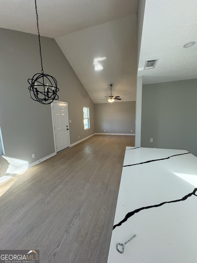 unfurnished living room with wood-type flooring, ceiling fan with notable chandelier, a textured ceiling, and vaulted ceiling