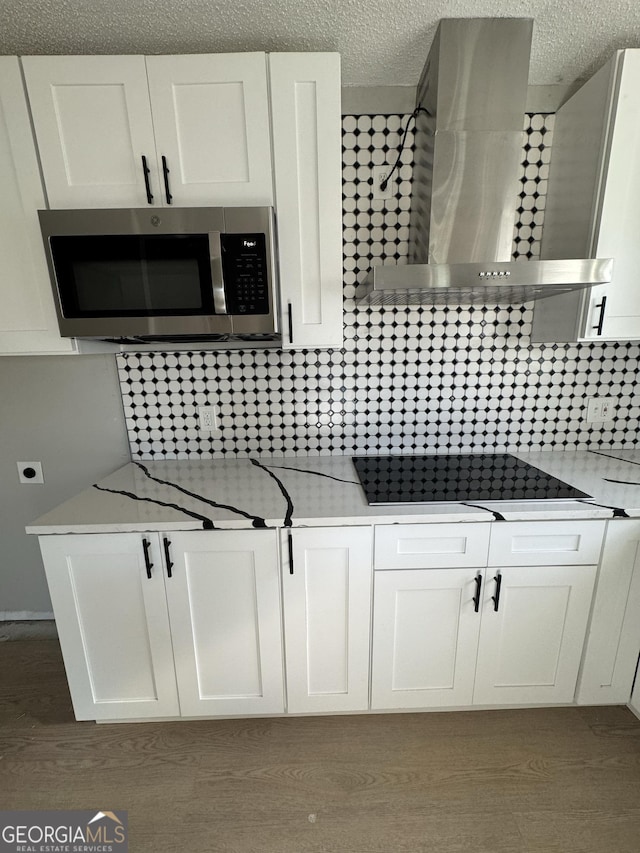 kitchen with light stone counters, wall chimney range hood, white cabinets, dark hardwood / wood-style floors, and black stovetop