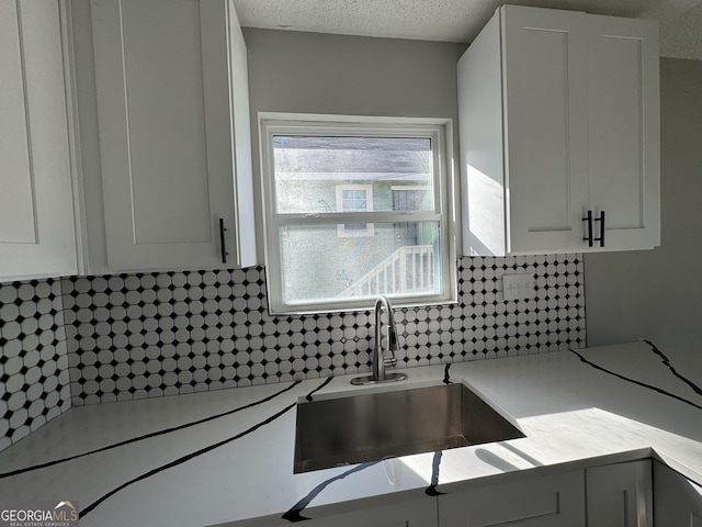 kitchen featuring decorative backsplash, a textured ceiling, white cabinetry, and sink