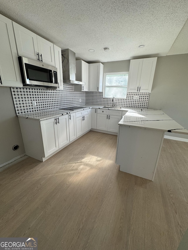 kitchen featuring wall chimney exhaust hood, light wood-type flooring, white cabinetry, and kitchen peninsula