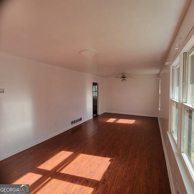 empty room featuring a wealth of natural light, dark wood-type flooring, and ceiling fan