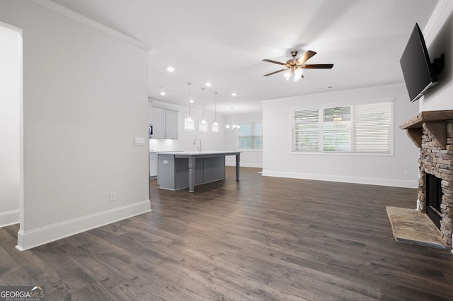 unfurnished living room featuring dark wood-type flooring, sink, ceiling fan, ornamental molding, and a fireplace