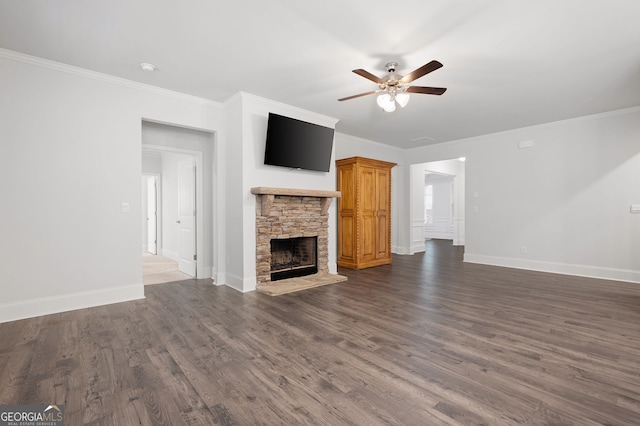 unfurnished living room featuring ceiling fan, a stone fireplace, dark hardwood / wood-style flooring, and crown molding