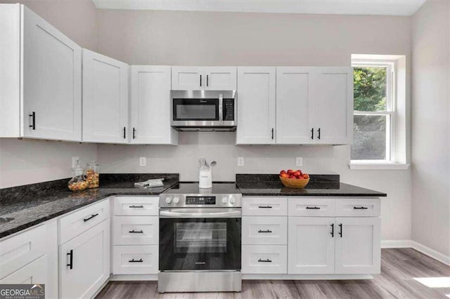 kitchen with light hardwood / wood-style floors, white cabinetry, dark stone counters, and appliances with stainless steel finishes