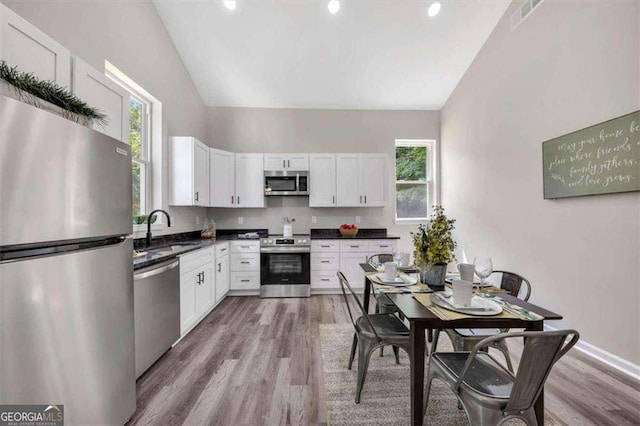 kitchen with stainless steel appliances, sink, light hardwood / wood-style flooring, white cabinets, and lofted ceiling