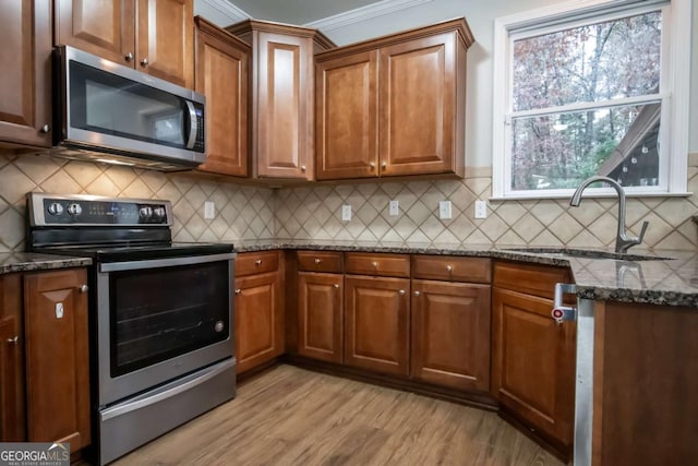 kitchen with sink, light hardwood / wood-style flooring, dark stone countertops, appliances with stainless steel finishes, and ornamental molding