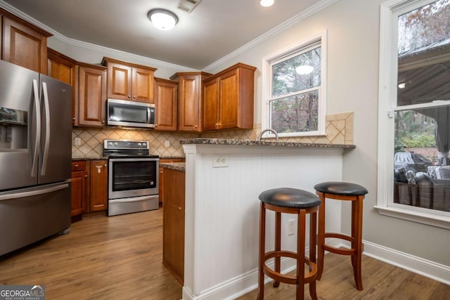 kitchen featuring a kitchen bar, stainless steel appliances, stone counters, and plenty of natural light