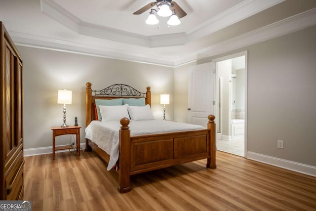 bedroom with ensuite bathroom, ornamental molding, a tray ceiling, ceiling fan, and wood-type flooring