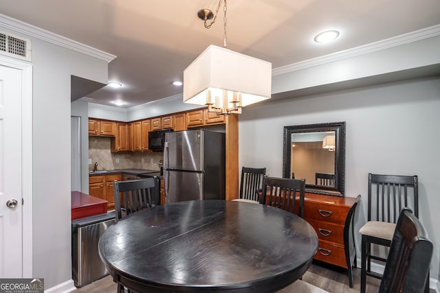 dining room with sink, crown molding, a chandelier, and hardwood / wood-style flooring