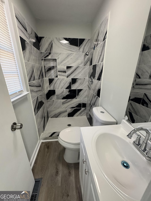 bathroom featuring tiled shower, hardwood / wood-style floors, vanity, and toilet