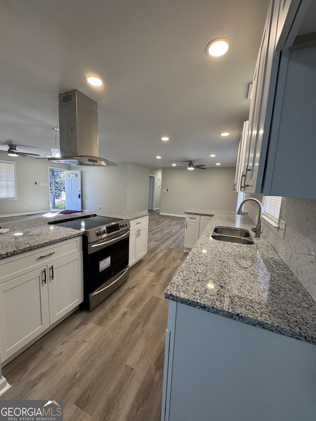 kitchen with stainless steel electric stove, white cabinetry, sink, and range hood