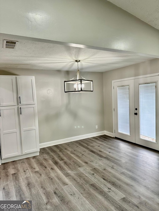 unfurnished dining area featuring french doors, a textured ceiling, an inviting chandelier, and light hardwood / wood-style flooring