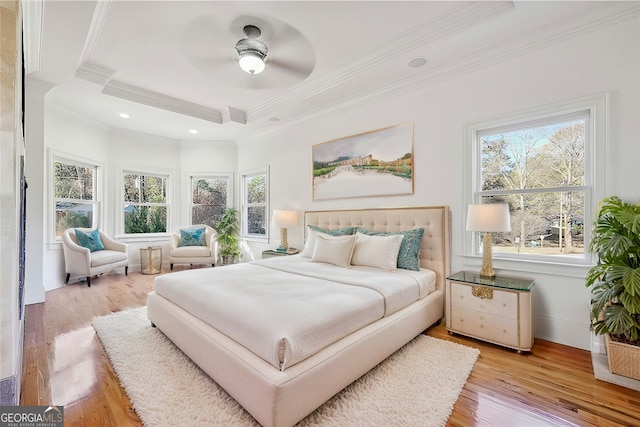 bedroom with multiple windows, a tray ceiling, ornamental molding, and light hardwood / wood-style floors