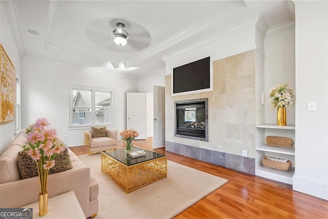 living room with a tiled fireplace, crown molding, hardwood / wood-style flooring, and ceiling fan