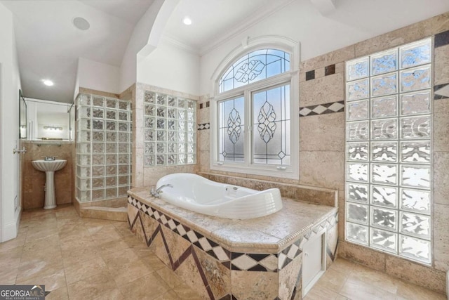 bathroom featuring ornamental molding, sink, tile walls, and a relaxing tiled tub