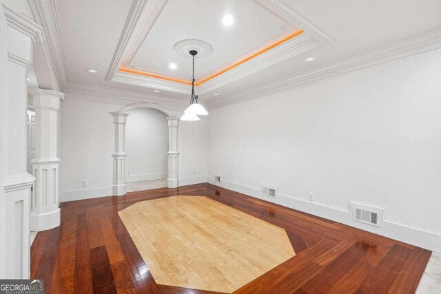 unfurnished dining area with dark wood-type flooring, ornamental molding, a tray ceiling, and decorative columns