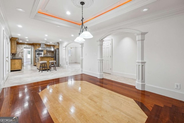 unfurnished dining area with ornamental molding, a raised ceiling, light hardwood / wood-style flooring, and ornate columns