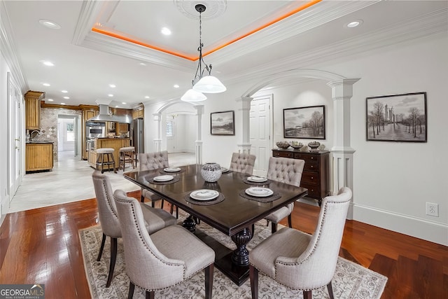 dining space with a tray ceiling, decorative columns, and light hardwood / wood-style floors