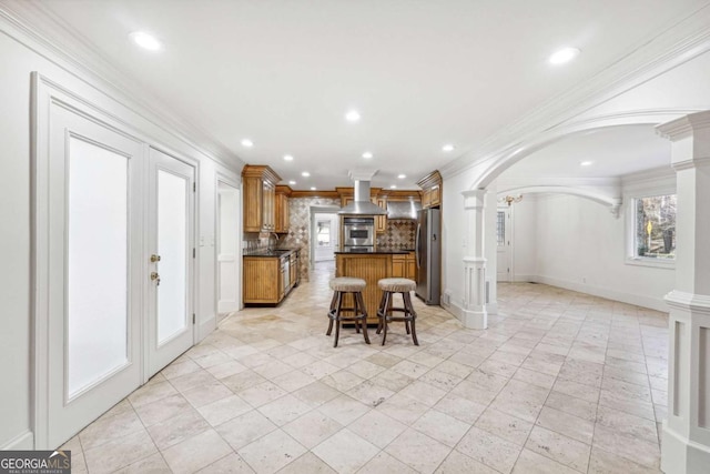 kitchen featuring stainless steel appliances, a kitchen bar, range hood, and decorative columns