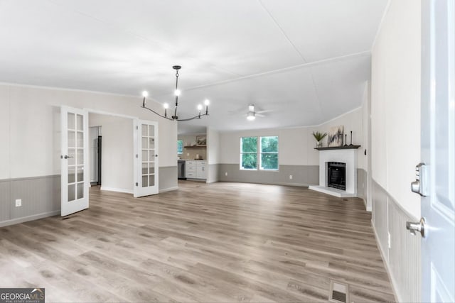 unfurnished living room with french doors, ceiling fan with notable chandelier, light hardwood / wood-style floors, and vaulted ceiling