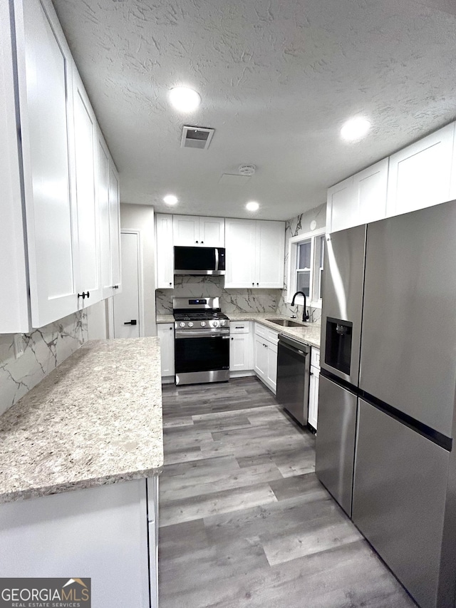 kitchen featuring backsplash, sink, appliances with stainless steel finishes, light hardwood / wood-style floors, and white cabinetry