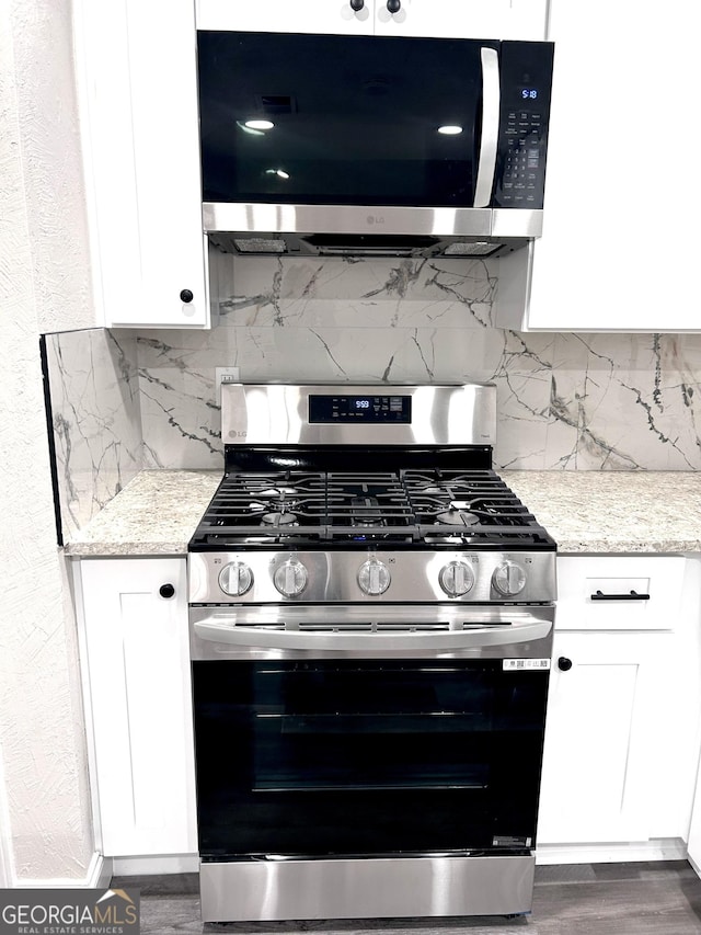 kitchen with tasteful backsplash, light stone counters, stainless steel appliances, dark hardwood / wood-style floors, and white cabinetry