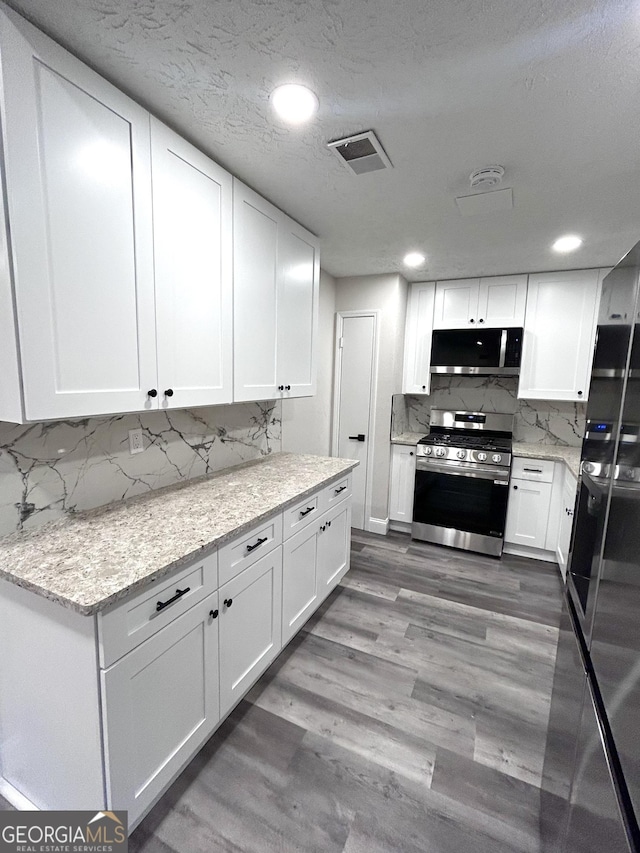 kitchen featuring light stone counters, backsplash, appliances with stainless steel finishes, white cabinets, and hardwood / wood-style flooring