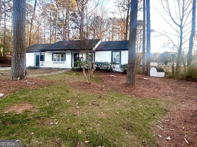 ranch-style house featuring covered porch, a storage unit, and a front yard