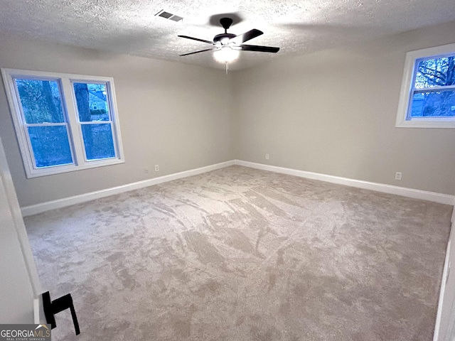 carpeted spare room with ceiling fan, a healthy amount of sunlight, and a textured ceiling