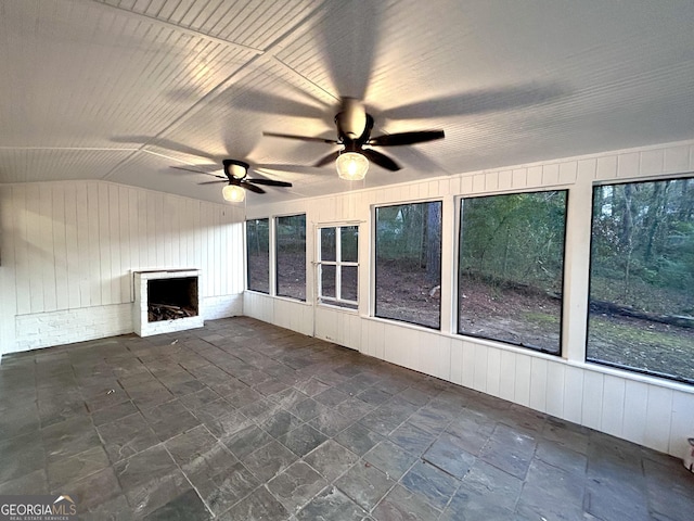 unfurnished sunroom with ceiling fan, a fireplace, a wealth of natural light, and vaulted ceiling