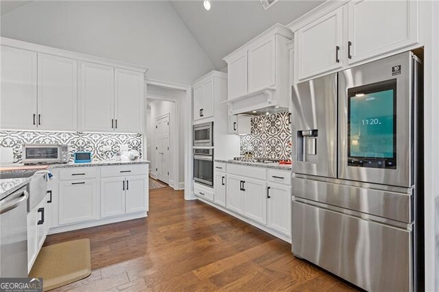 kitchen with dark hardwood / wood-style flooring, backsplash, light stone counters, stainless steel appliances, and white cabinetry