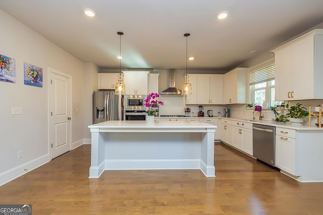 kitchen with wall chimney exhaust hood, stainless steel appliances, a kitchen island, white cabinetry, and hanging light fixtures