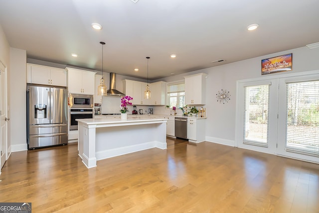 kitchen with wall chimney exhaust hood, a healthy amount of sunlight, a kitchen island, and stainless steel appliances