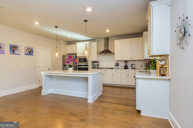 kitchen featuring hardwood / wood-style floors, wall chimney range hood, a kitchen island, white cabinetry, and stainless steel appliances