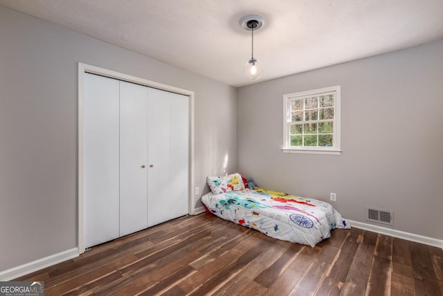 unfurnished bedroom featuring a closet, baseboards, visible vents, and wood finished floors