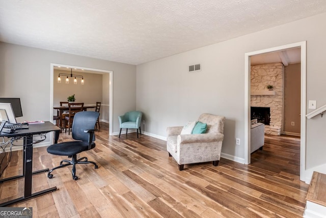 home office featuring baseboards, a textured ceiling, visible vents, a stone fireplace, and wood finished floors