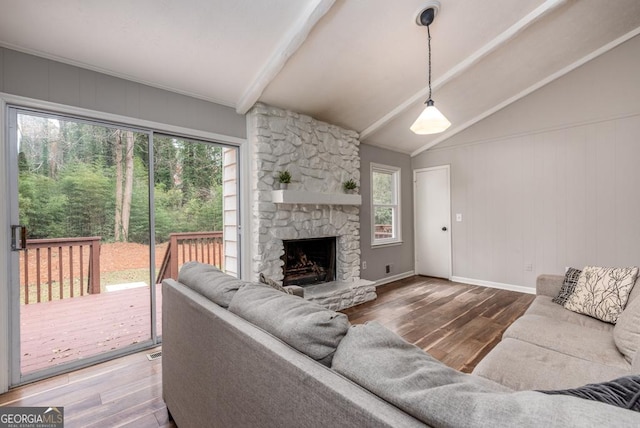 living area featuring lofted ceiling with beams, baseboards, wood finished floors, and a stone fireplace