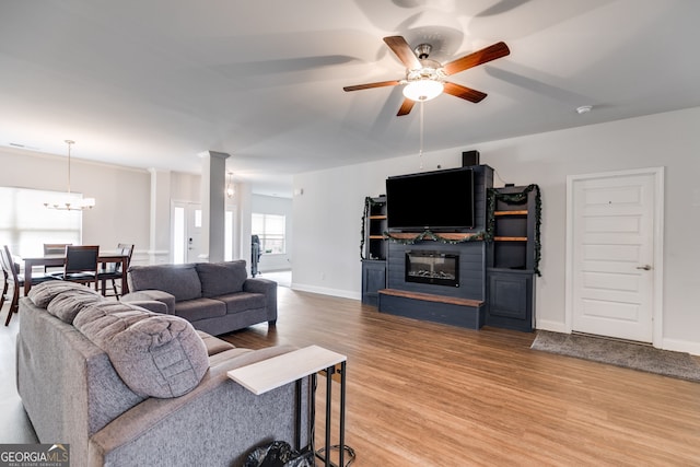 living room featuring ceiling fan with notable chandelier, a fireplace, hardwood / wood-style floors, and ornate columns