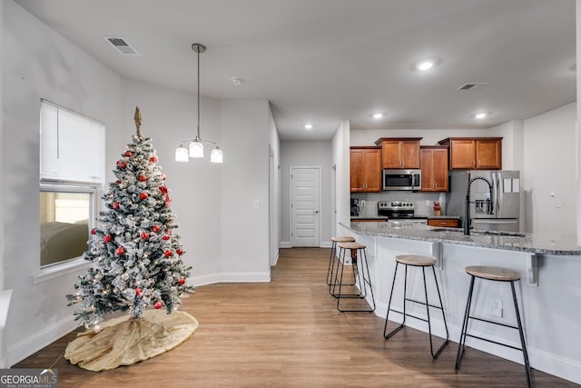 kitchen featuring appliances with stainless steel finishes, decorative light fixtures, a kitchen bar, decorative backsplash, and light stone counters