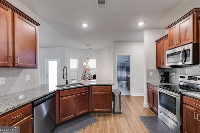 kitchen featuring sink, decorative light fixtures, light hardwood / wood-style flooring, appliances with stainless steel finishes, and light stone countertops