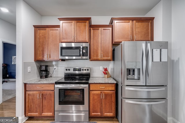 kitchen featuring stainless steel appliances, backsplash, light stone counters, and light hardwood / wood-style floors