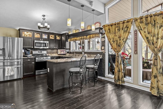 kitchen with dark hardwood / wood-style floors, decorative backsplash, light stone countertops, appliances with stainless steel finishes, and decorative light fixtures