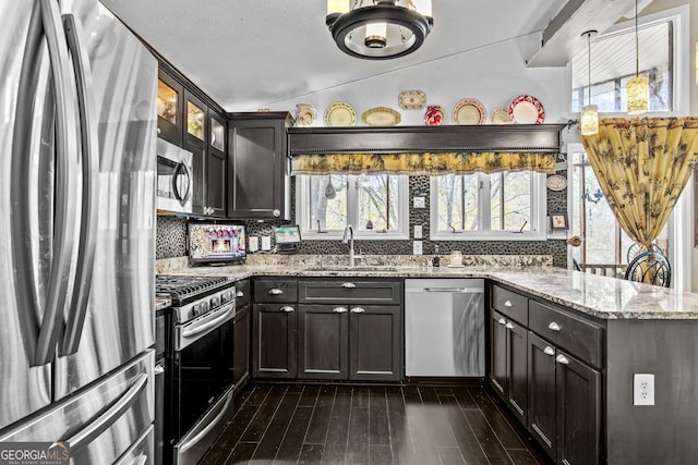 kitchen with light stone countertops, appliances with stainless steel finishes, vaulted ceiling, sink, and decorative light fixtures