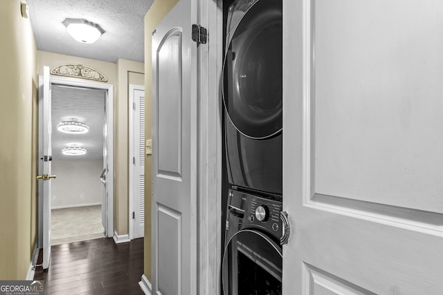 laundry area featuring a textured ceiling, dark wood-type flooring, and stacked washer / drying machine