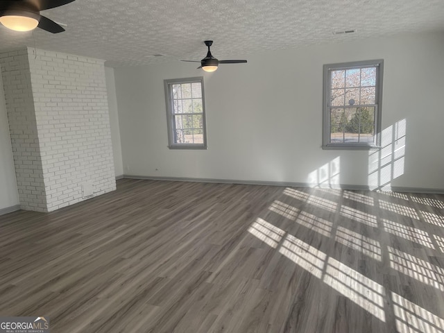 unfurnished living room with ceiling fan, dark wood-type flooring, a wealth of natural light, and a textured ceiling