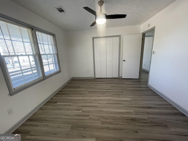 unfurnished bedroom with ceiling fan, a textured ceiling, dark hardwood / wood-style floors, and a closet