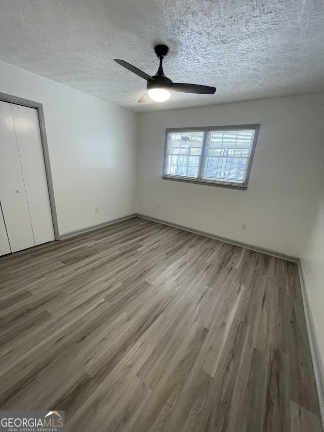 unfurnished bedroom featuring ceiling fan, a textured ceiling, hardwood / wood-style flooring, and a closet