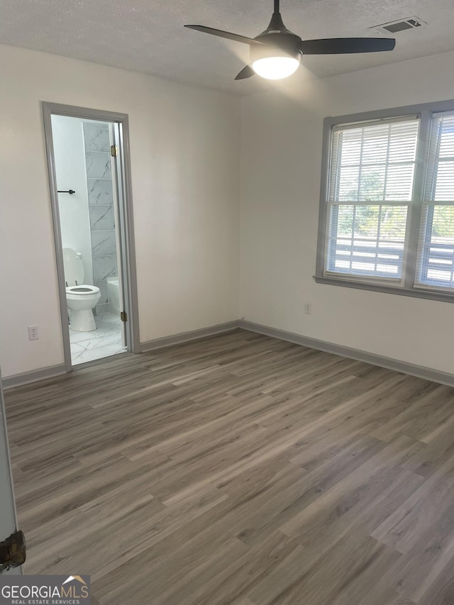 unfurnished bedroom with a textured ceiling, ceiling fan, dark hardwood / wood-style floors, and ensuite bath