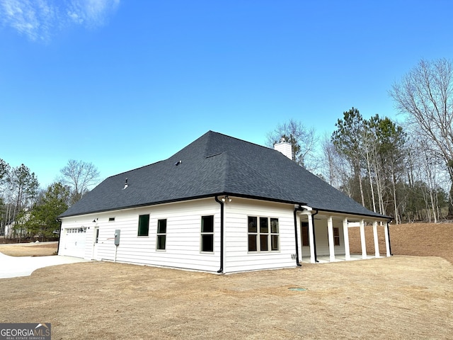 rear view of property with a shingled roof, concrete driveway, a chimney, and an attached garage